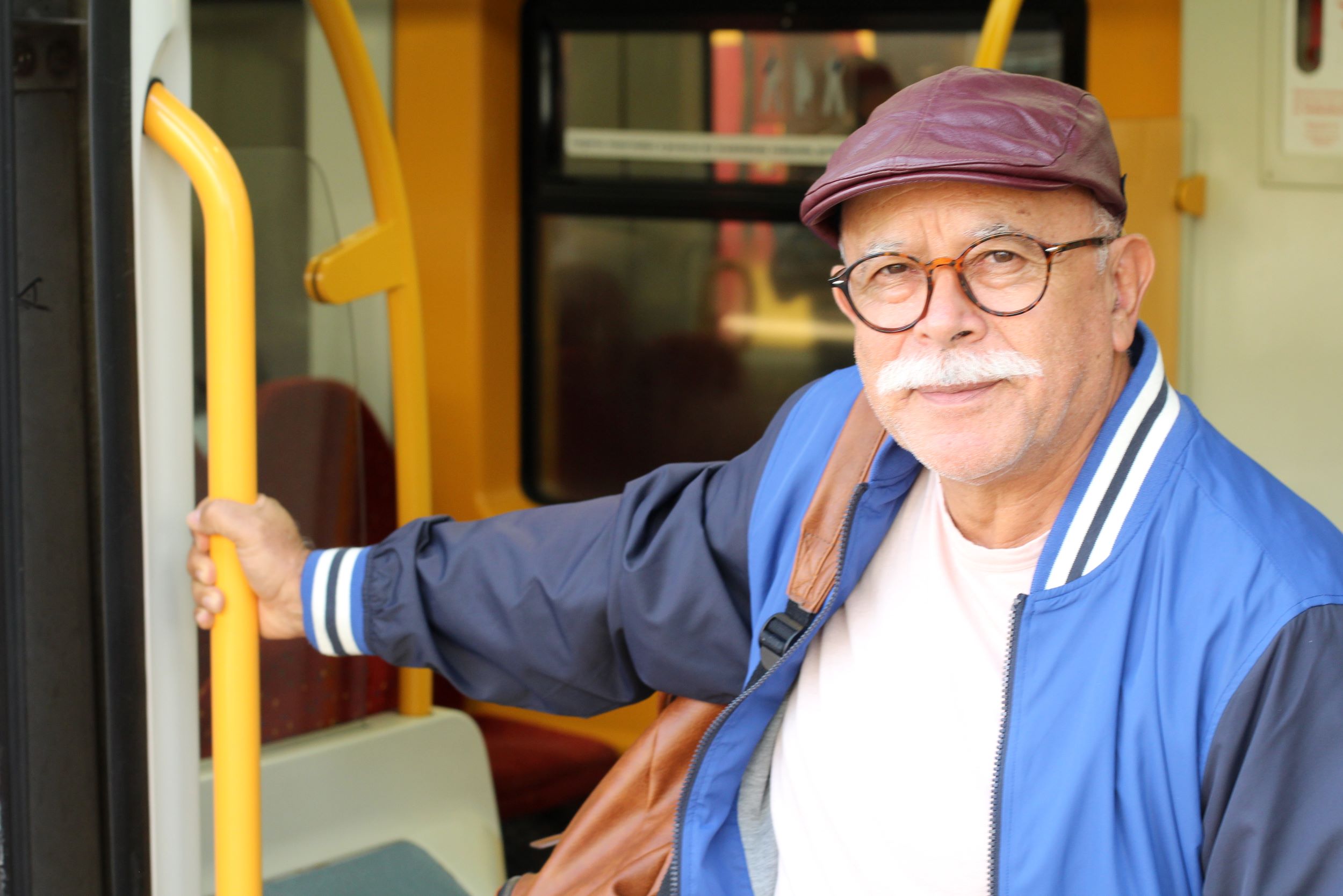A man looking at the camera, slightly smiling. He's getting off a bus and holding the rail