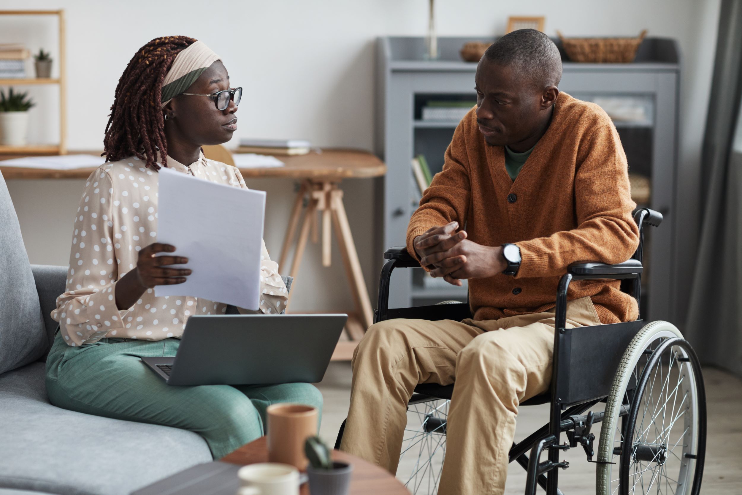 A couple young looking at papers and using a laptop. The man is in a wheelchair
