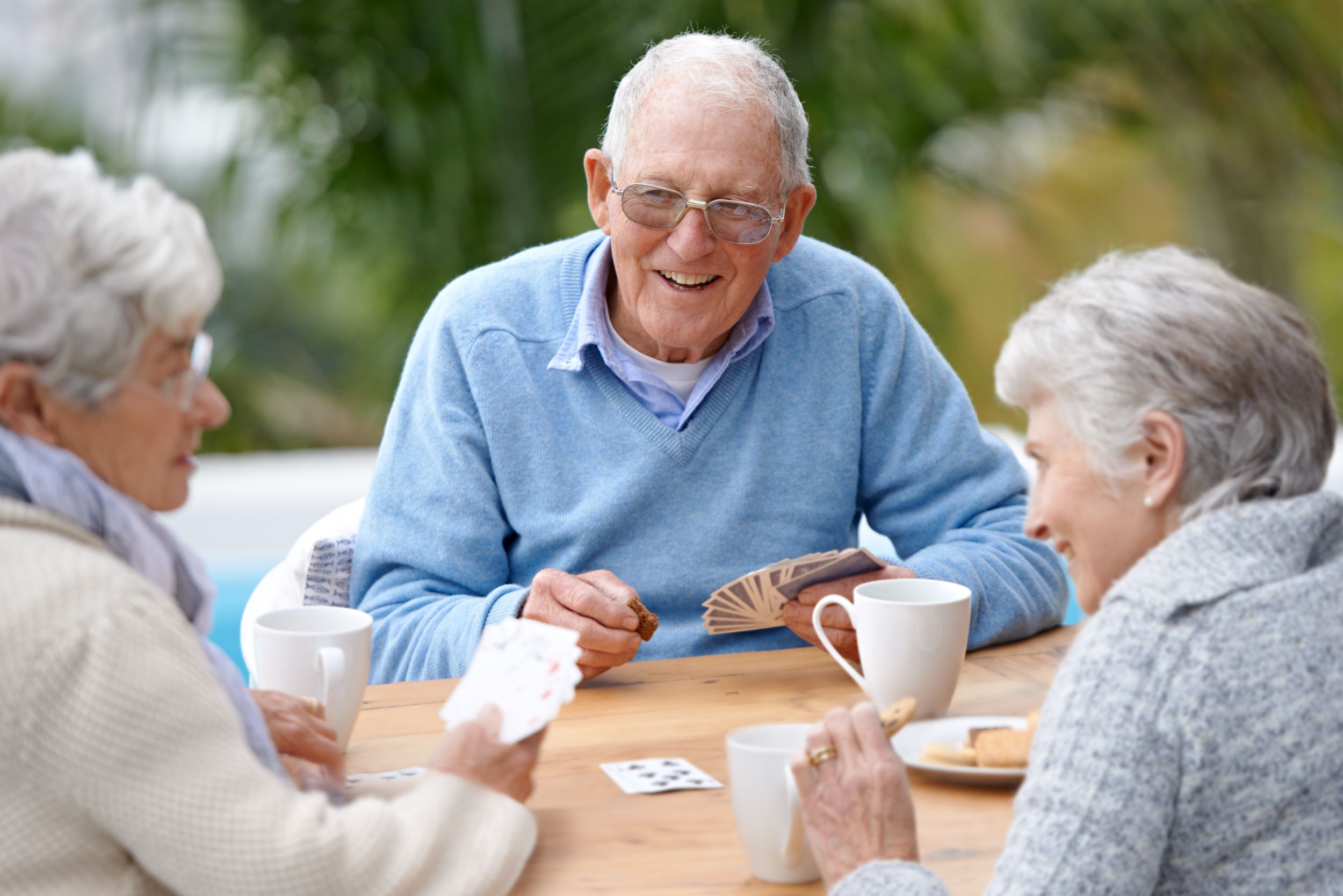 A man and two women playing cards, drinking tea and eating biscuits outside
