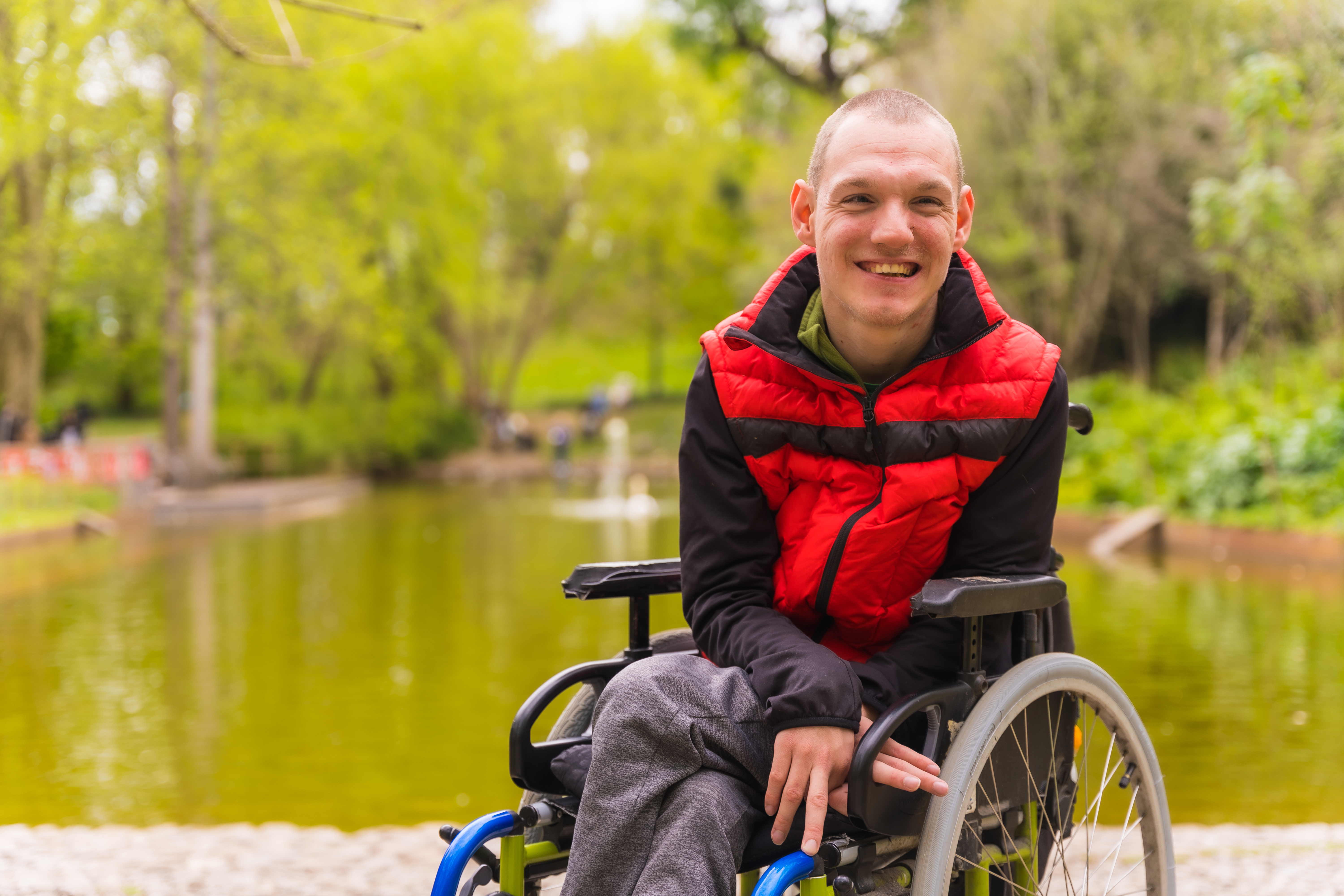 A man in a wheelchair smiling beside a lake