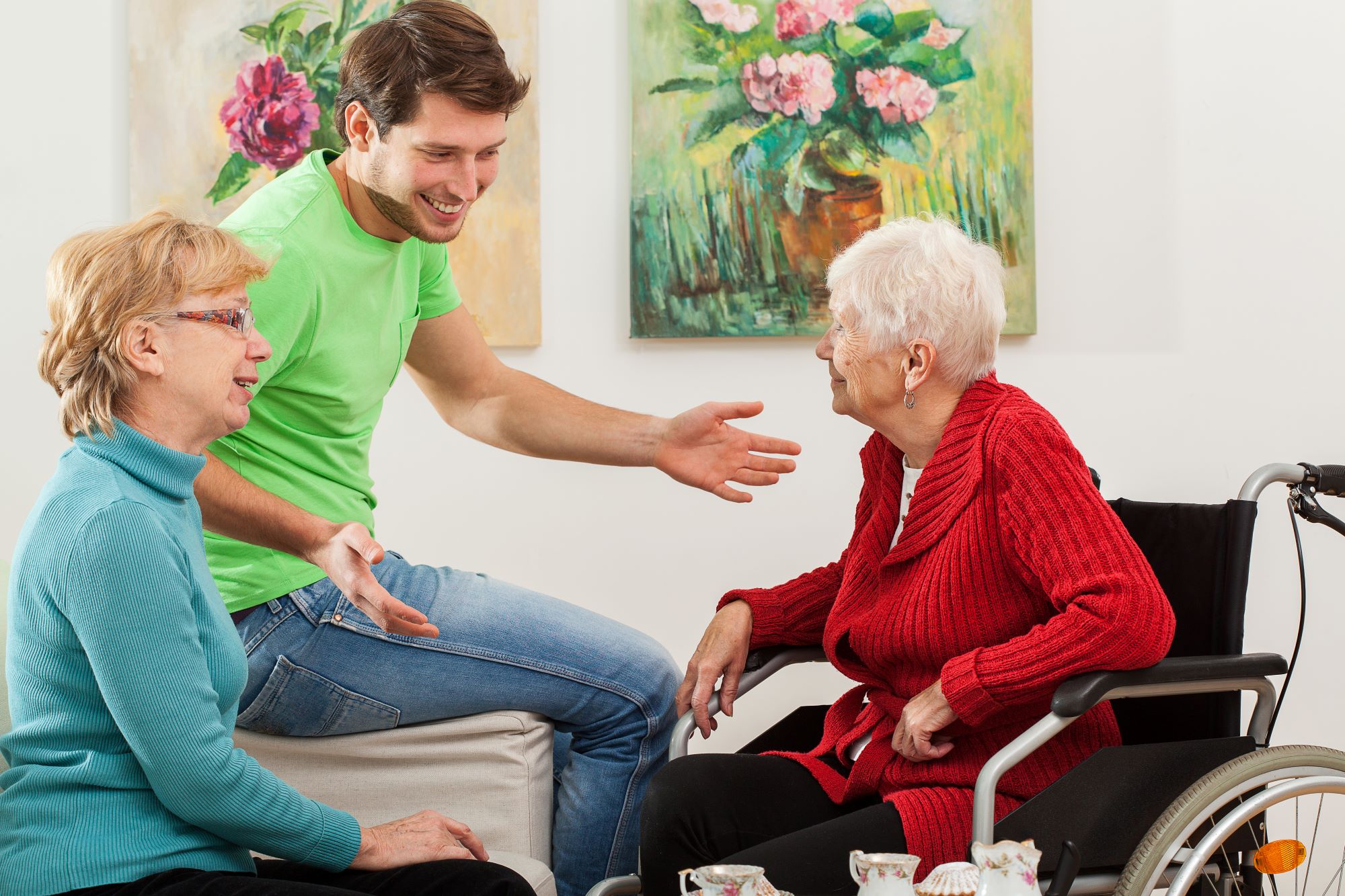 Three generations of people talking and smiling. One is in a wheel chair, the others are sitting on a sofa