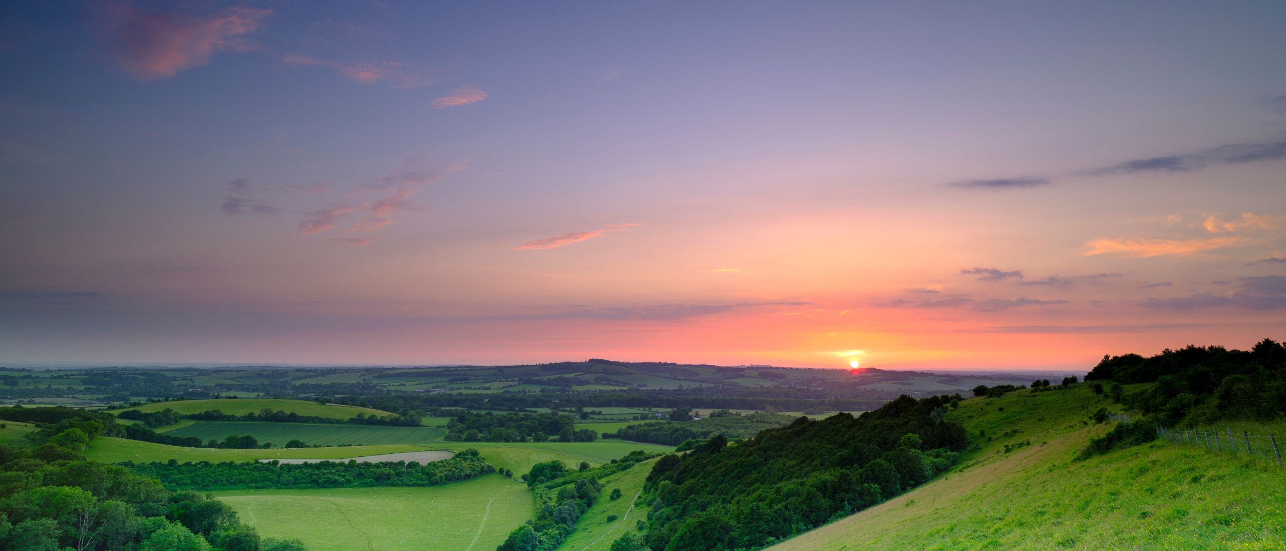 A pink and purple sunset over a green hill