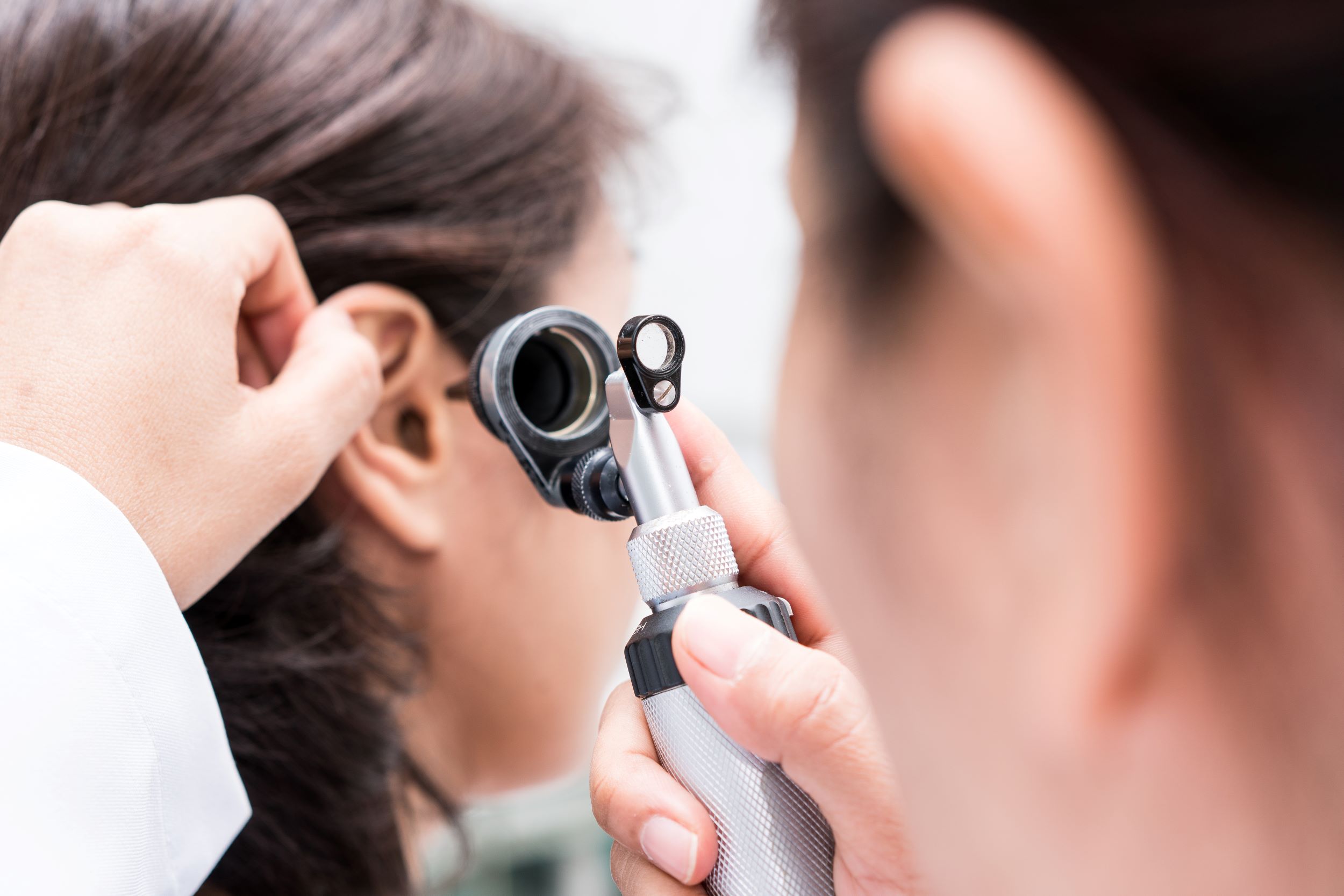 A medical professional checking a woman's ear with magnifying equipment
